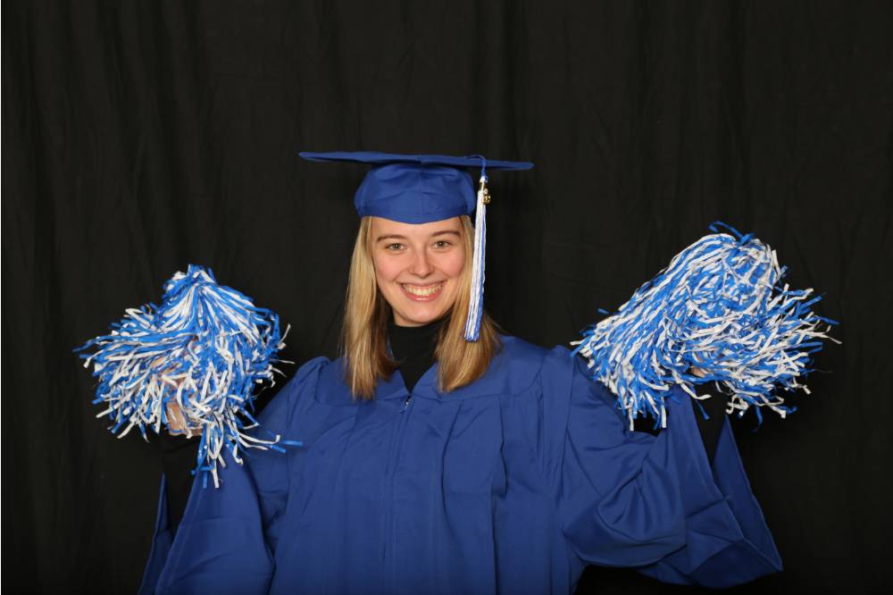 student in cap and gown with pom poms